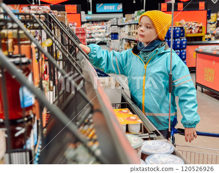 A boy in a yellow cap and blue jacket is shopping at a market. A child with a productive basket in a market. Shopping. 120526926