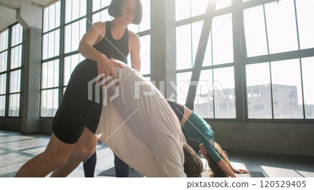 Sport class. Yoga studio. Group people training stretch lesson downward facing dog asana on mat with female coach fitness instructor help correcting pose in gym indoors. 120529405