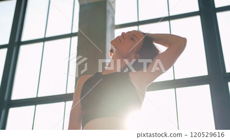 Body warm-up. Neck stretching. Athletic woman in activewear side tilt head with hands training spine muscle in light fitness studio interior. Body warm-up. Neck stretching. Athletic woman in activewear side tilt head with hands training spine muscle in light fitness studio interior. 120529616