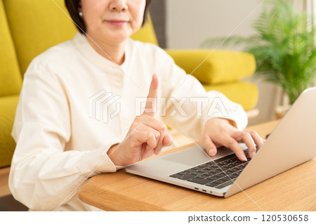 中高級女性在客廳觸摸電腦並舉起食指 中高級女性在客廳觸摸電腦並舉起食指 120530658