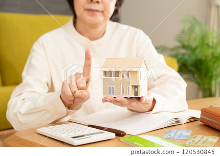 A middle-aged woman who is managing her household finances and raising her index finger with a house model 120530845
