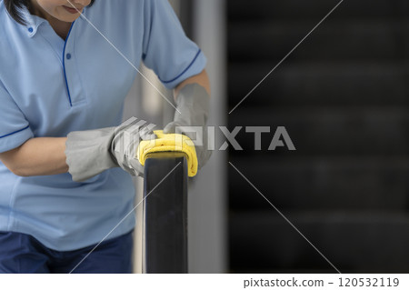 The hands of a cleaning staff member wiping the handrail of an escalator 120532119