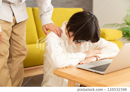 A middle-aged couple looking down in front of a computer in the living room 120532396