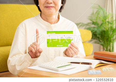 中高級婦女拿著銀行存摺，微笑著指著她的食指和家庭帳本 120532610