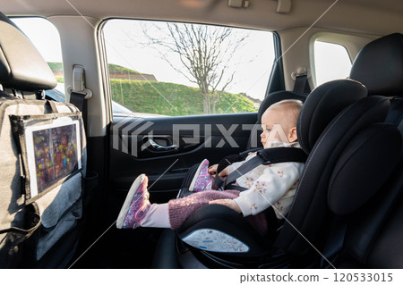Toddler in car seat watching screen on road trip. Concept of safe family travel and engaging children 120533015