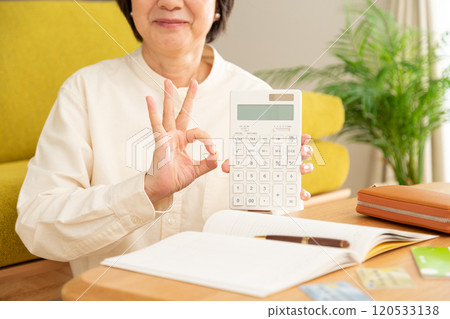 A middle-aged woman holding a calculator and making a circle sign and a household account book 120533138
