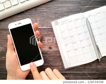 Hands operating a smartphone and a schedule book 120534598