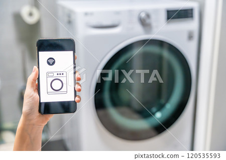 Young woman using mobile phone control via wi-fi and app for washing machine in home. Homesmart and new technology concept Young woman using mobile phone control via wi-fi and app for washing machine in home. Homesmart and new technology concept 120535593