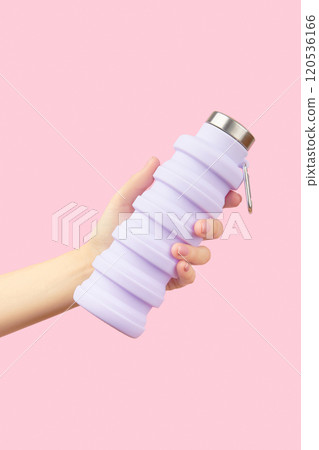 Womans hand holding collapsible reusable lilac water bottle on pink background. Sustainable lifestyle Womans hand holding collapsible reusable lilac water bottle on pink background. Sustainable lifestyle 120536166