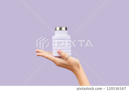 Womans hand holding collapsible reusable lilac water bottle on purple background. Zero waste Womans hand holding collapsible reusable lilac water bottle on purple background. Zero waste 120536167