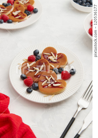 A heap of heart shaped pancakes with berries and cutlery on the white plate on grey background 120536177