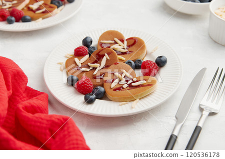 A heap of heart shaped pancakes with berries and cutlery on the white plate on grey background A heap of heart shaped pancakes with berries and cutlery on the white plate on grey background 120536178