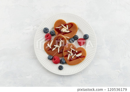 A heap of heart shaped pancakes with berries on the white plate on the grey background 120536179