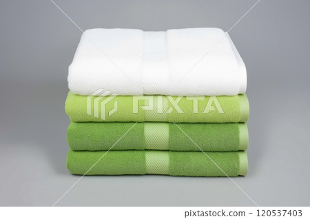 Green and white towels stacked in even layers on a gray surface, showcasing crisp and soft textures 120537403