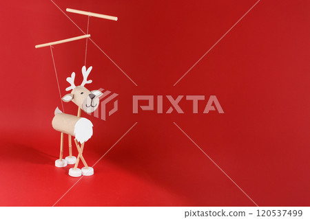 DIY toilet paper roll craft for kids featuring homemade reindeer marionette toy from recycled materials. Easy New Year craft and children's activity idea. Creative holiday project, red backdrop, 120537499