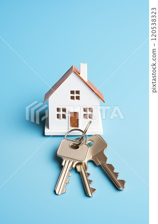 Miniature house model with three metal keys placed in front, set against a clean blue backdrop 120538323