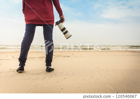 Woman walking on beach with camera 120540067
