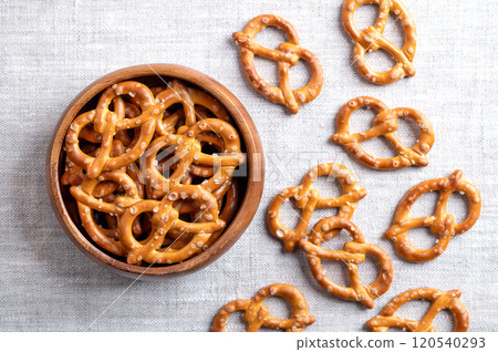 Salted pretzels in a wooden bowl on linen fabric. Golden toasted small pretzels of traditional shape with ends intertwined to form a pretzel bow, made of wheat flour, used for snacking and dipping. Salted pretzels in a wooden bowl on linen fabric. Golden toasted small pretzels of traditional shape with ends intertwined to form a pretzel bow, made of wheat flour, used for snacking and dipping. 120540293