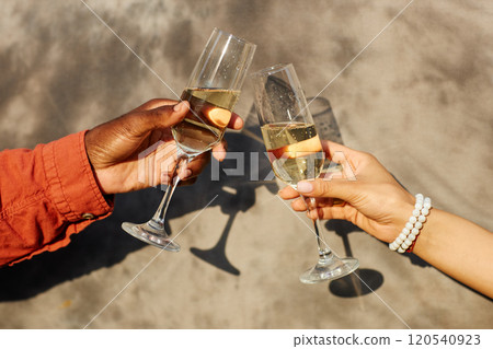 Close-up of two hands clinking champagne glasses during celebration, with shadows cast on wall behind creating an elegant and joyful scene 120540923
