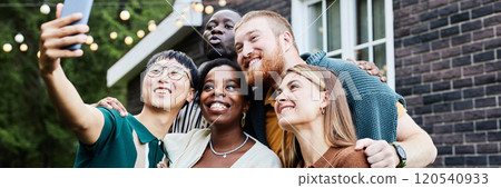 Waist up portrait of multiethnic group of people taking selfie photo together outdoors by house decorated with fairy lights Waist up portrait of multiethnic group of people taking selfie photo together outdoors by house decorated with fairy lights 120540933