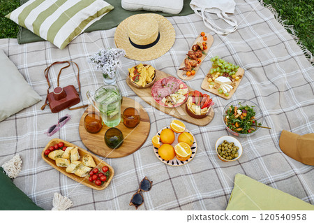 Picnic setup on plaid blanket with various snacks, fruits, and drinks Creating inviting atmosphere for outdoor meal 120540958