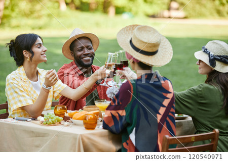 Group of friends enjoying picnic outdoors, sharing food and drinks in sunny park setting. Celebrating with cheerful faces, sitting around picnic table Group of friends enjoying picnic outdoors, sharing food and drinks in sunny park setting. Celebrating with cheerful faces, sitting around picnic table 120540971