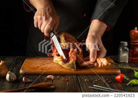 In the cozy kitchen, an experienced chef expertly slices the flavorful meat of a poultry carcass with a sharp knife. Aromatic ingredients surround the wooden table, enhancing the culinary experience In the cozy kitchen, an experienced chef expertly slices the flavorful meat of a poultry carcass with a sharp knife. Aromatic ingredients surround the wooden table, enhancing the culinary experience 120541923