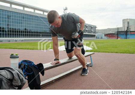 Exercising with Dumbbell Outdoors by Athletic Man 120542184