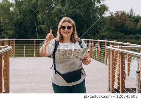 Stylish hipster 30s woman in sunglasses wearing backpack pointing finger, relaxing in nature. Travel and wanderlust concept. Amazing chill moment 120543608