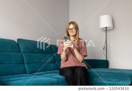 Beautiful blonde woman having fun online on her smartphone at home or hotel. Phone Communication and comfort concept. Smiling 30s woman daydreaming and holding mobile phone with copy space. Beautiful blonde woman having fun online on her smartphone at home or hotel. Phone Communication and comfort concept. Smiling 30s woman daydreaming and holding mobile phone with copy space. 120543610