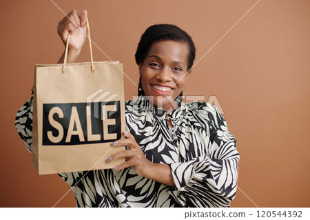 Smiling Woman Holding Sale Bag against Brown Background 120544392