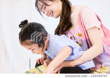 A nursery teacher reading a picture book with a child A nursery teacher reading a picture book with a child 120544747