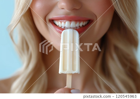 Close up of a blonde woman smiling brightly, showing teeth while holding a creamy white popsicle 120545963