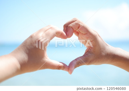 Hands forming a heart shape with the sea in the background. 120546080