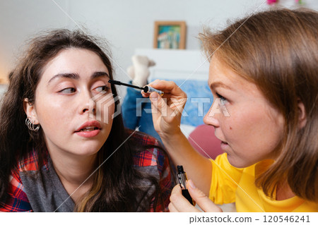 Two young women make up decorative cosmetics. One woman paints another woman's eyelashes with mascara. The concept of LGBT relationships and makeup Two young women make up decorative cosmetics. One woman paints another woman's eyelashes with mascara. The concept of LGBT relationships and makeup 120546241