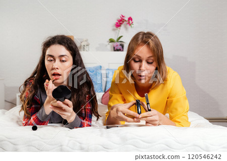 Two young women lie on the bed and make up with cosmetics. The concept of LGBT relationships and self care Two young women lie on the bed and make up with cosmetics. The concept of LGBT relationships and self care 120546242