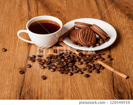 A cup of coffee, a plate of chocolate cookies, cinnamon stickers. Roasted coffee beans. 120549559