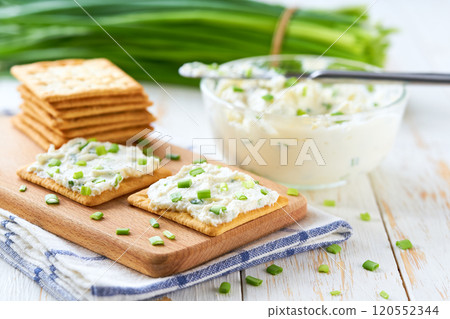 Glass bowl of cream cheese with  spring onions and crackers, on a wooden table, selective focus. 120552344