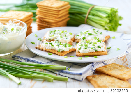 Crispy crackers and a glass bowl with a cream cheese spread and cut chives on a light kitchen table. Crispy crackers and a glass bowl with a cream cheese spread and cut chives on a light kitchen table. 120552353