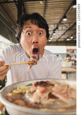 Happy and excited face man eating Moo Kra Ta or Thai BBQ buffet. 120552469