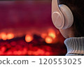 Alone sad woman in headphones sitting and warming at winter evening near fireplace flame and  christmas tree. 120553025