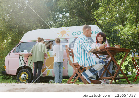 Low angle shot of biracial people enjoying meal at table while unrecognizable couple making order in background Low angle shot of biracial people enjoying meal at table while unrecognizable couple making order in background 120554338