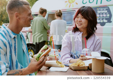Medium close up of biracial couple sitting at table smiling and enjoying tasty meal under open sky 120554339