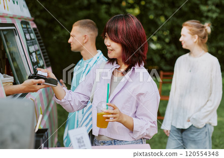 Asian smiling customer tapping card to pay for craft lemonade bought in food truck Asian smiling customer tapping card to pay for craft lemonade bought in food truck 120554348
