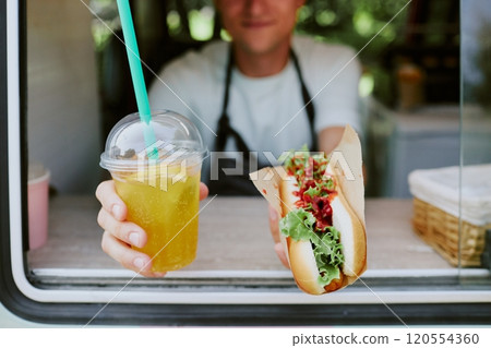 Medium close up of fresh made citrus lemonade and fresh cooked hot dog in hands of unrecognizable chef Medium close up of fresh made citrus lemonade and fresh cooked hot dog in hands of unrecognizable chef 120554360