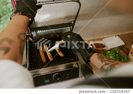 High angle shot f unrecognizable chef cutting sausages while they frying on grill in food truck High angle shot f unrecognizable chef cutting sausages while they frying on grill in food truck 120554397