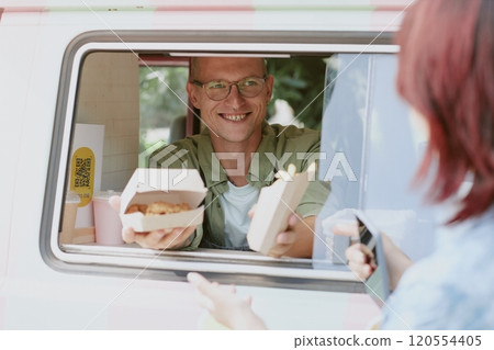 Medium close up of happy and smiling cook of food truck holding box of nuggets and french fries 120554405