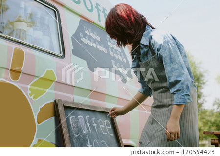 Low angle shot of unrecognizable female worker in stripped apron writing down coffee menu on blackboard 120554423