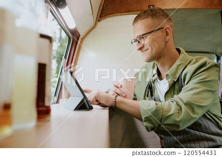 Smiling Caucasian worker of food truck texting in social network while having break at work Smiling Caucasian worker of food truck texting in social network while having break at work 120554431