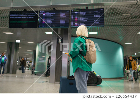 Caucasian senior woman passengers with suitcase using mobile phone booking hotel during waiting flight at boarding gate in airport terminal. Attractive female tourist travel by airplane on holiday Caucasian senior woman passengers with suitcase using mobile phone booking hotel during waiting flight at boarding gate in airport terminal. Attractive female tourist travel by airplane on holiday 120554437
